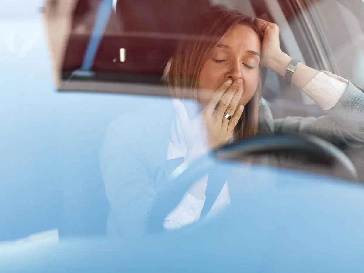 Mujer bostezando en el coche. Para disminuir la probabilidad de somnolencia debe evitar conducir.