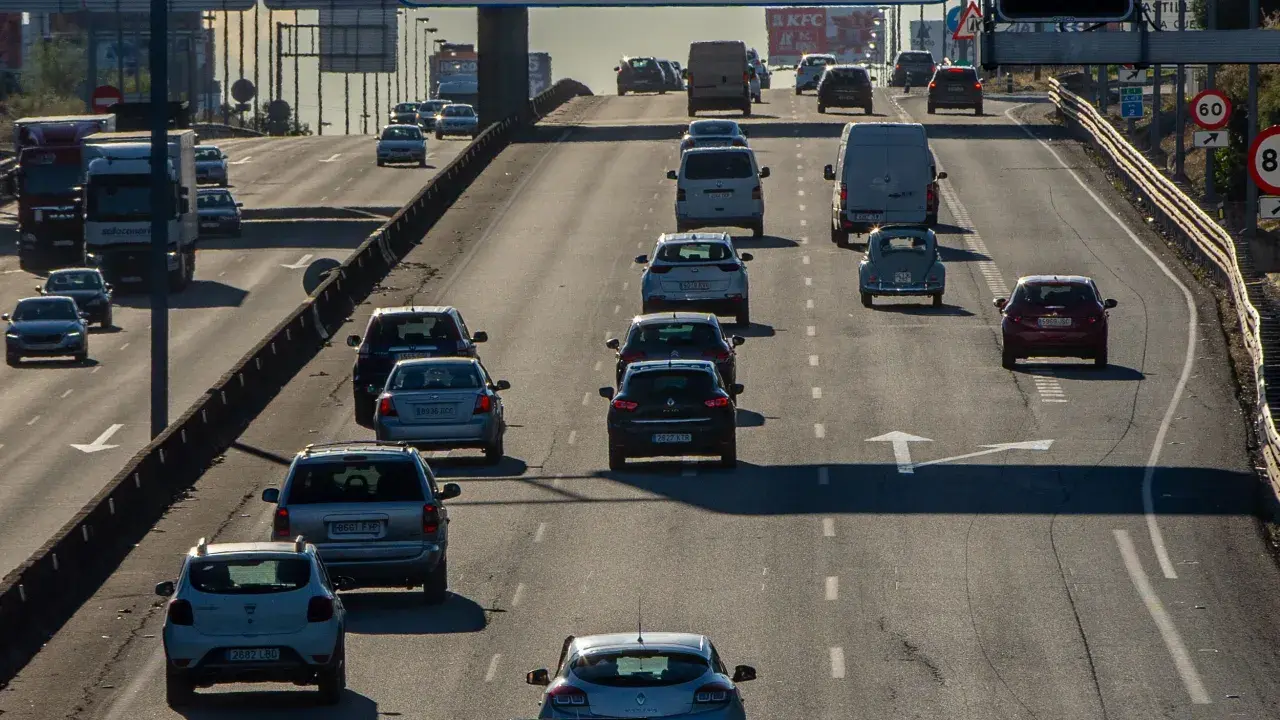 Tráfico denso en autopista, con coches y furgonetas circulando. Se observa señal de tráfico con **mínimo de velocidad en autopista** de 60 km/h.