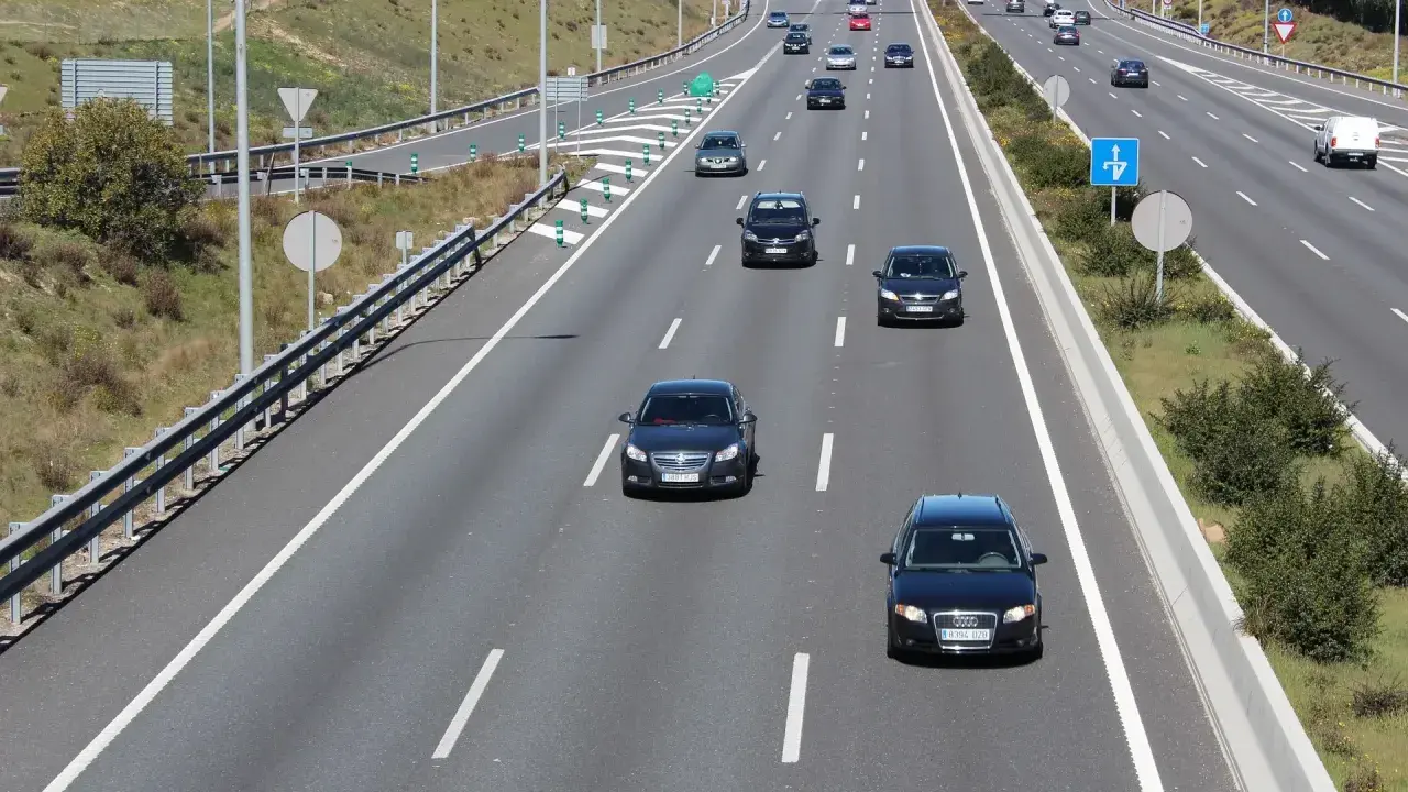 En el carril de entrada, ¿cómo debe circular? Un coche negro circula por el carril de entrada de una autopista, con otros vehículos delante y detrás.