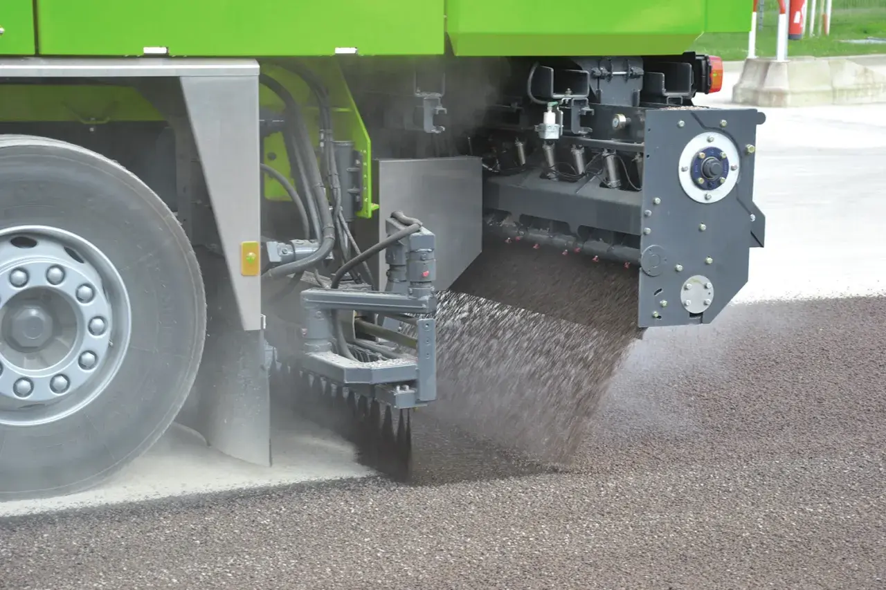 Máquina esparciendo material granular sobre el asfalto, parte de un proceso de reciclado.