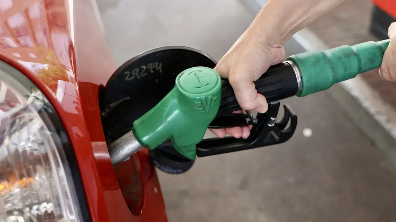Mano repostando un coche rojo con una manguera de combustible verde. El futuro de los coches diésel aún depende de la gasolina.