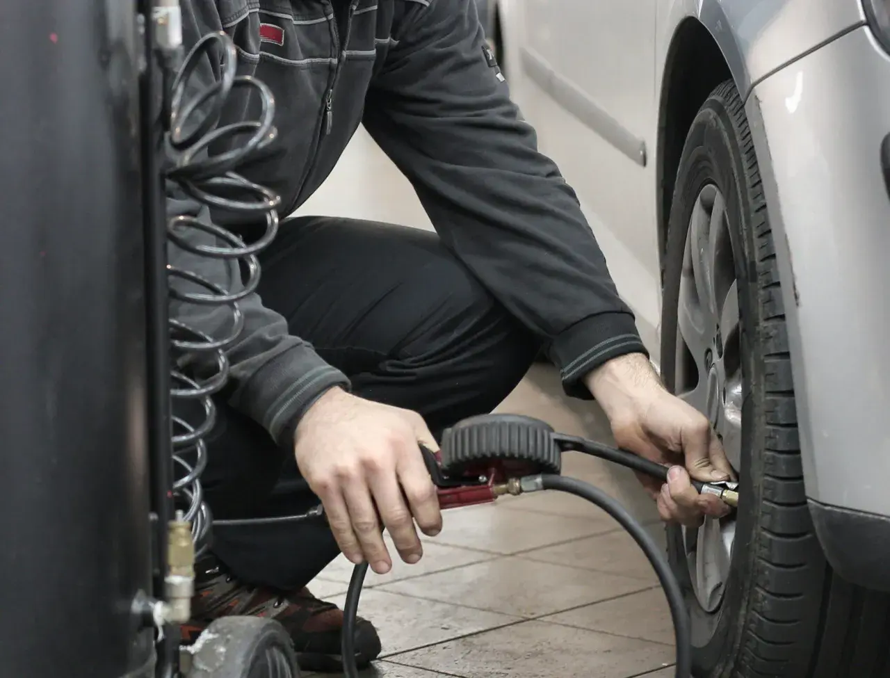 Hombre agachado conectando una manguera a la válvula de un neumático para reparar pinchazo coche.
