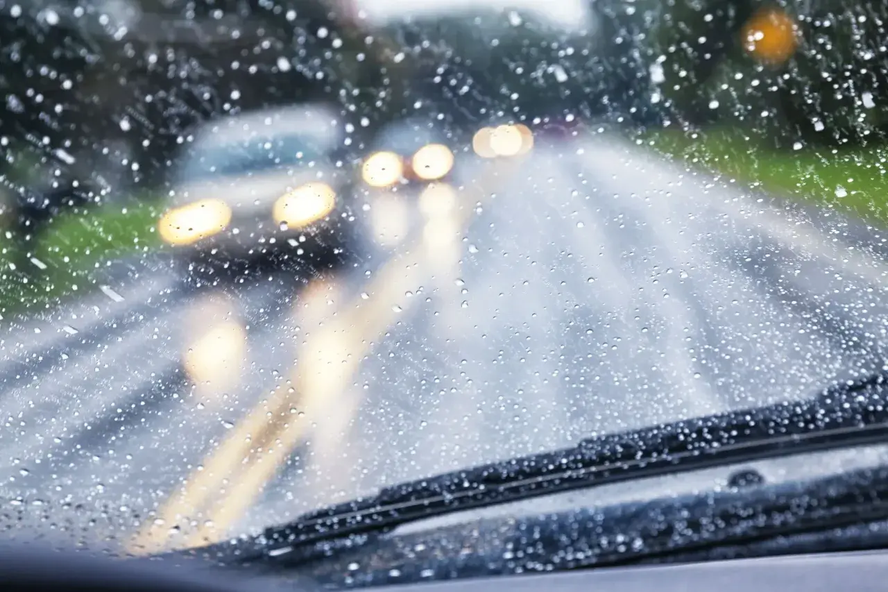 Si conduciendo le sorprende una lluvia torrencial, el parabrisas se llena de gotas. Luces de otros coches se difuminan en la carretera mojada.