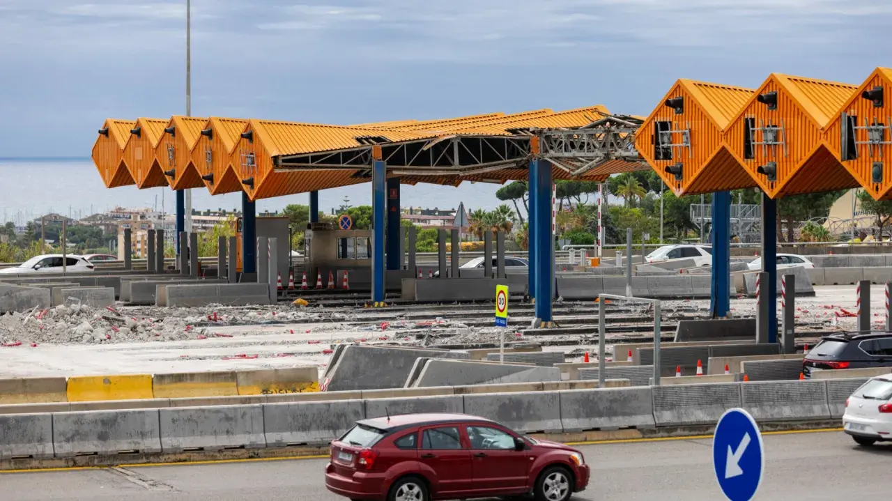 Peaje en construcción cerca de Barcelona. Estructuras naranjas y azules, escombros y coches circulan.