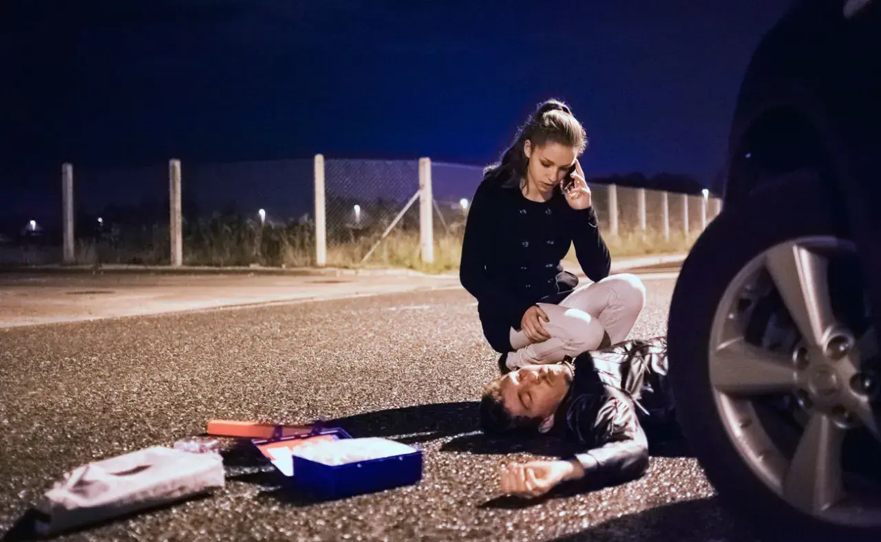 Una mujer llama a emergencias junto a un hombre tendido en la carretera. A su lado, un botiquín abierto. ¿Qué significa pas? ¿Una vida en peligro?