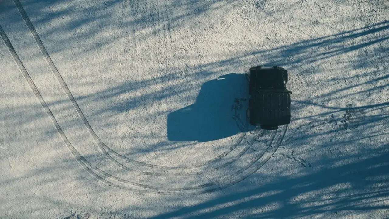 Un vehículo negro deja huellas en la nieve, mostrando cómo conducir con hielo.
