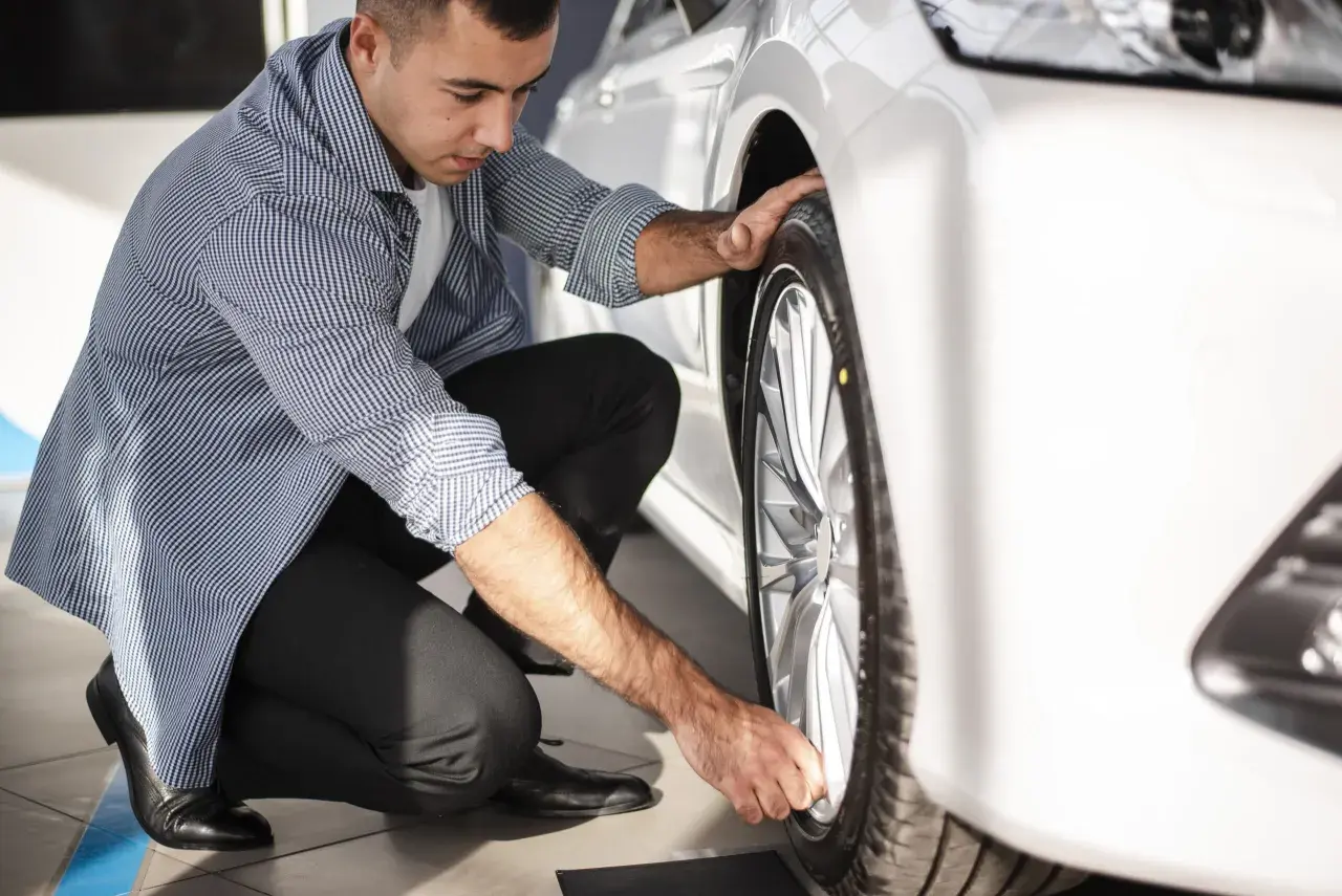 Hombre revisando la rueda de un coche blanco, asegurándose de que el neumático tenga el código velocidad correcto para un viaje seguro.