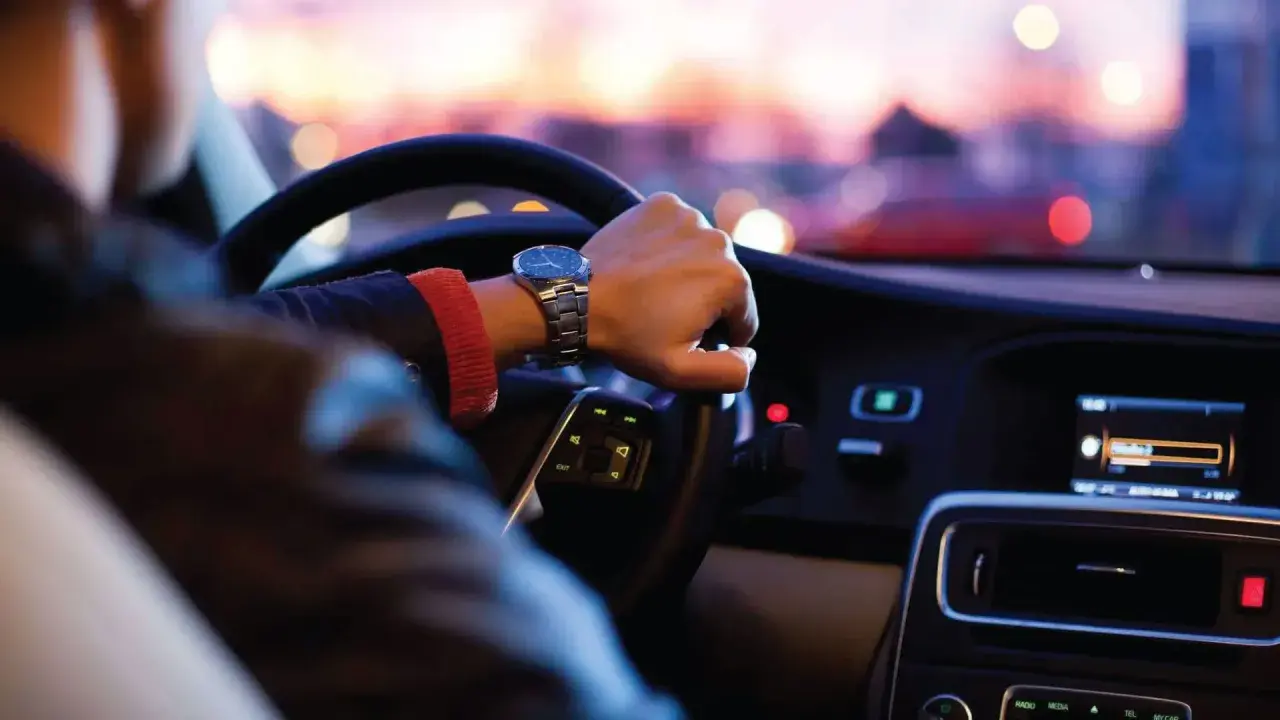 Persona conduce de noche en EE.UU., atento al **límite de velocidad** y al tráfico urbano.
