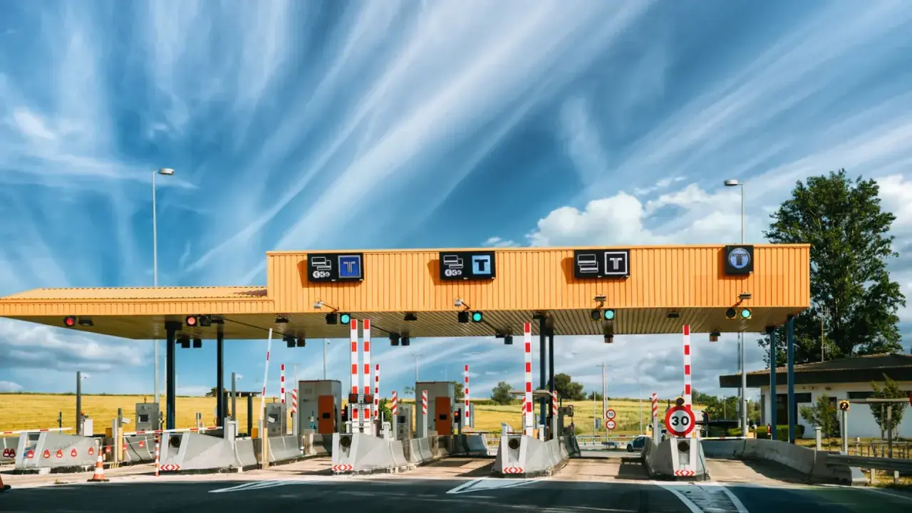 Estación de ap2 peajes bajo un cielo azul con nubes. Carriles de pago con barreras y señales de tráfico.