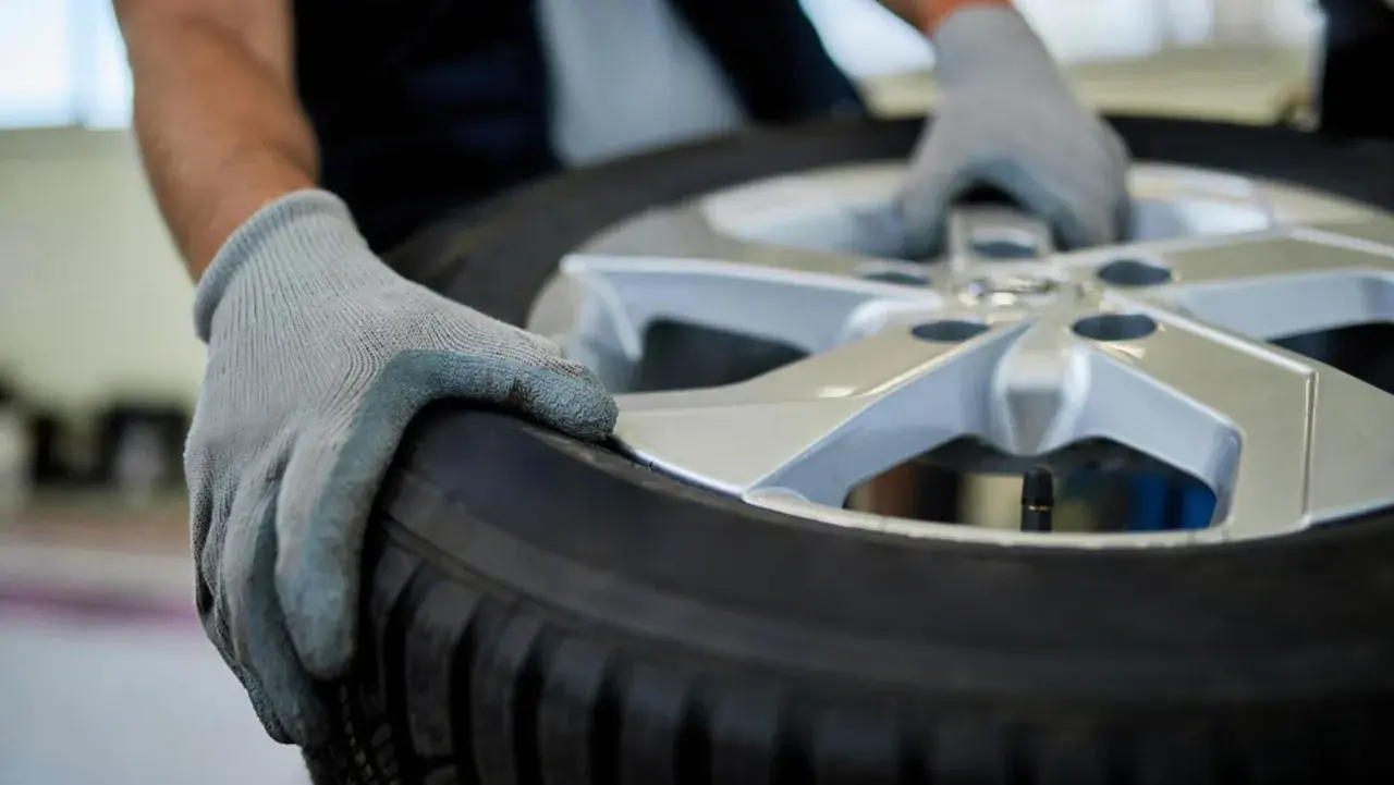 Manos enguantadas sostienen un neumático y llanta, listos para su reparación.