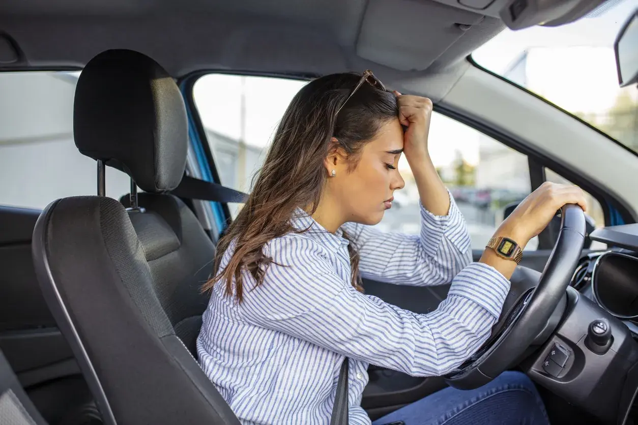 Mujer con la mano en la frente, sufriendo ansiedad al conducir.