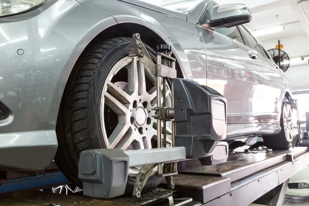 Un coche plateado en un taller mecánico recibe servicio de alineación de ruedas con equipo especializado.