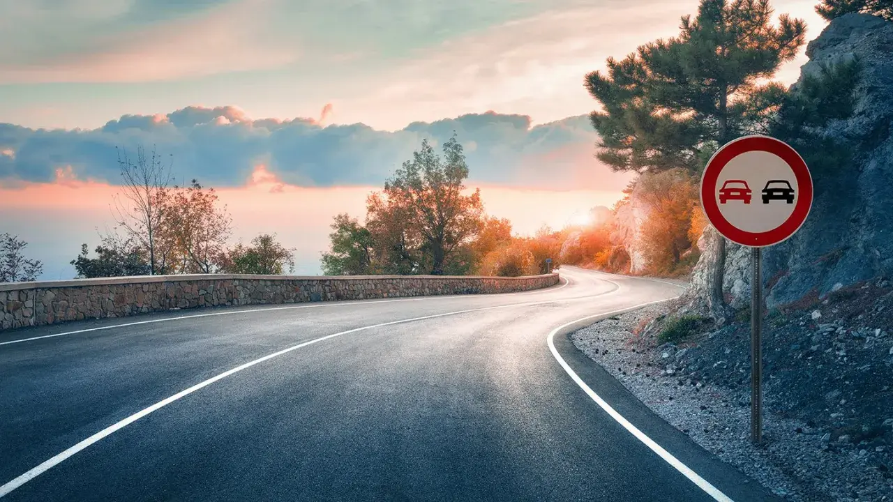 Carretera sinuosa al atardecer. Señal de prohibido adelantar en curvas.