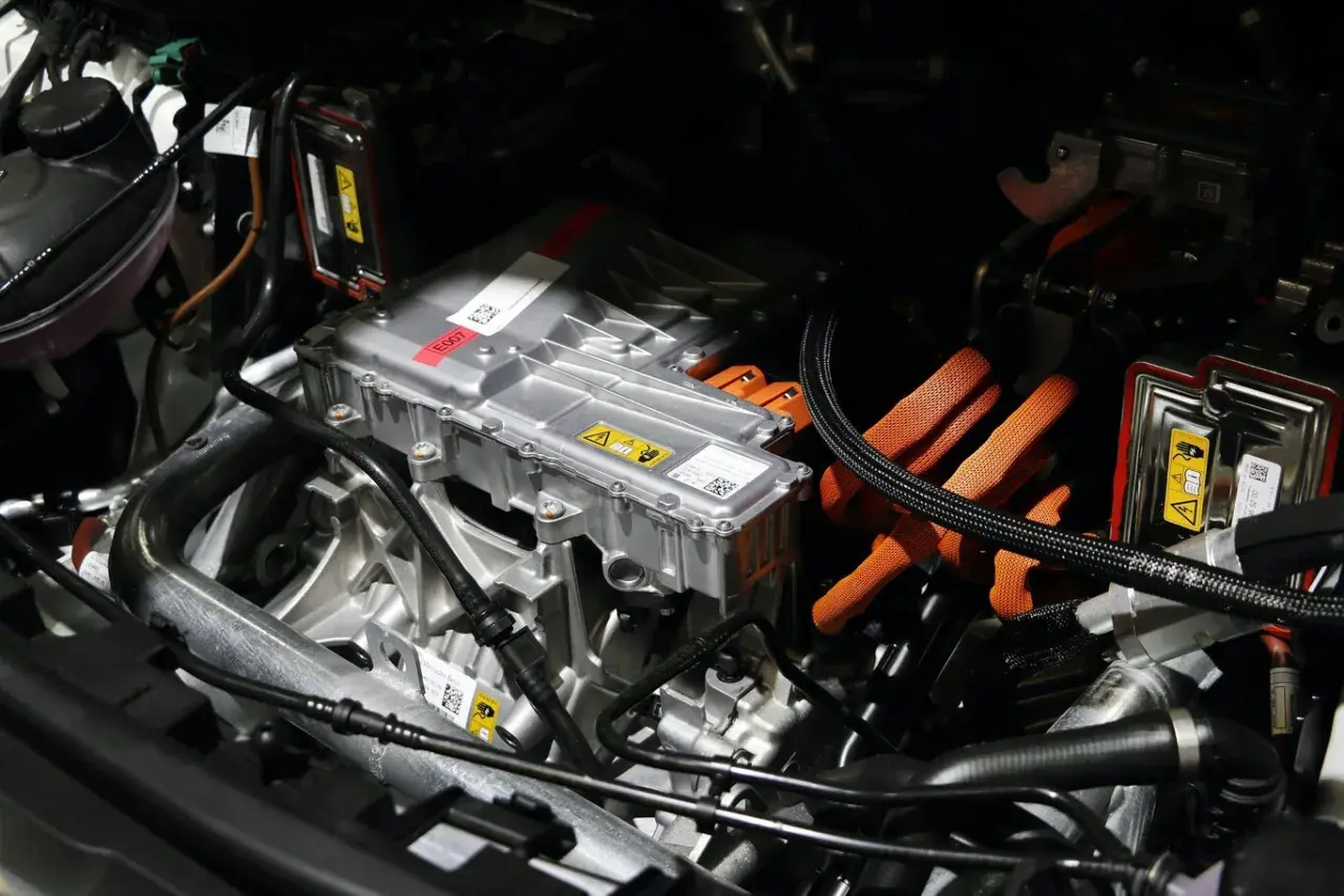 Detalles del motor de un coche eléctrico, listo para su revisión. Cables naranjas de alta tensión y componentes metálicos.