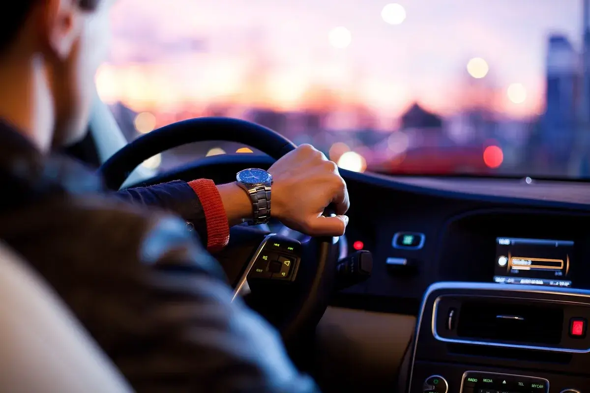 Hombre con reloj conduce a mayor velocidad, con luces de ciudad borrosas al atardecer.