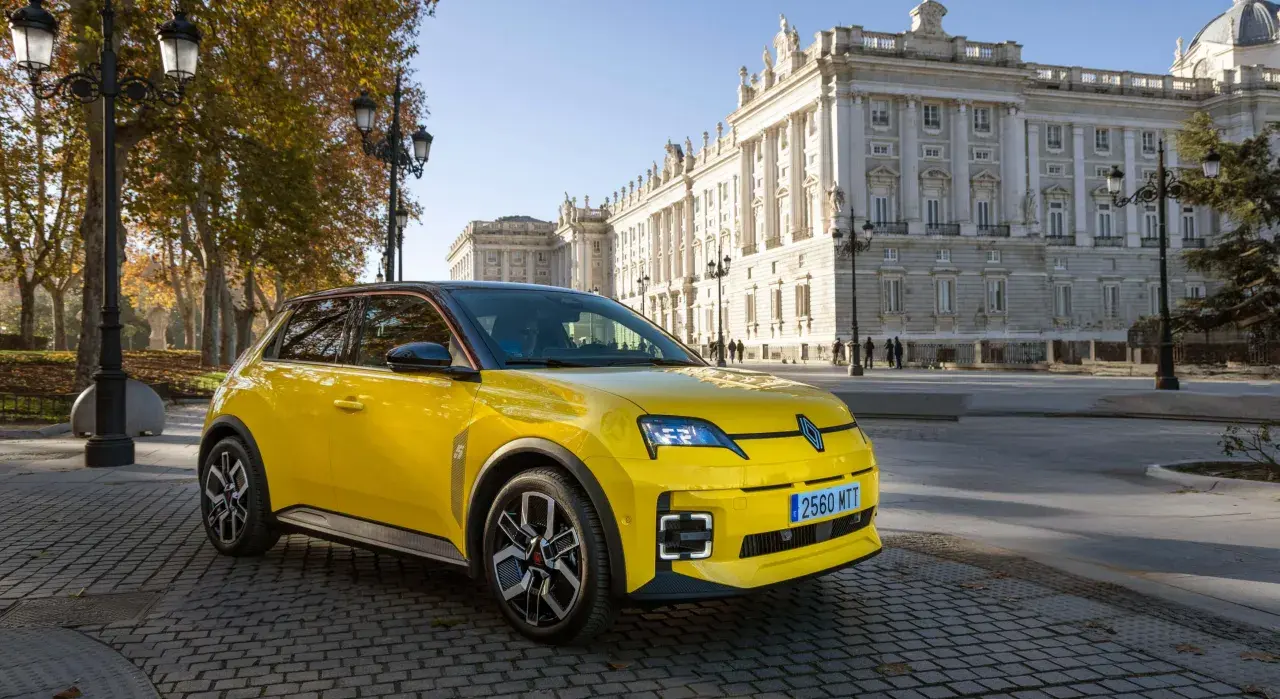 Coche amarillo con etiqueta ECO, aparcado frente a un edificio histórico. Los coches con etiqueta eco pagan impuesto de circulación, pero este parece disfrutar de un día soleado.