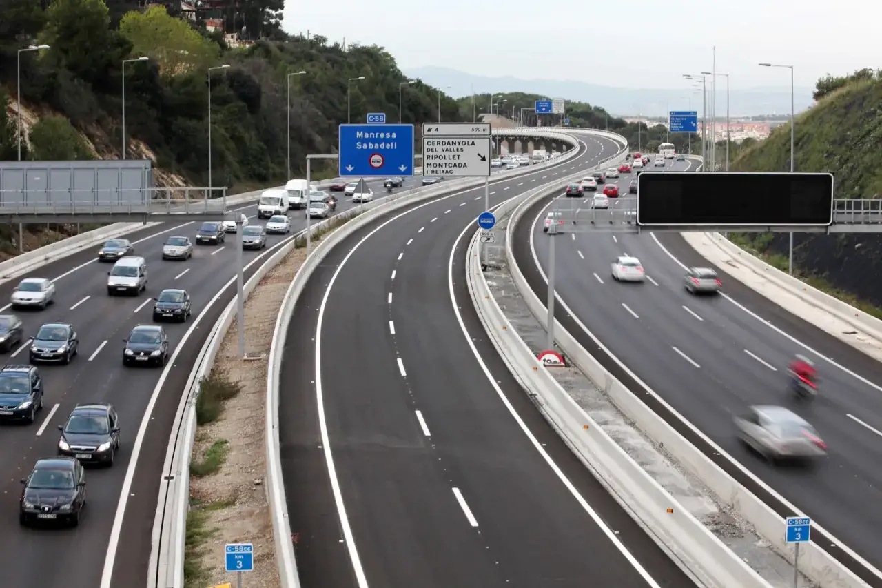 Tr&aacute;fico en la autopista C-58, v&iacute;a de acceso a vao Barcelona. Coches y furgonetas circulan por carriles amplios rodeados de vegetaci&oacute;n.