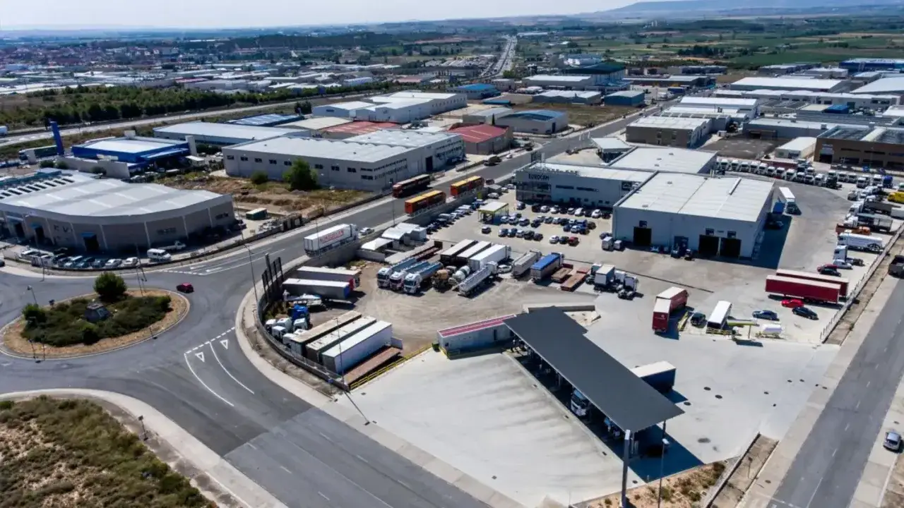 Vista aérea de un gran aparcamiento de camiones con múltiples naves industriales y vehículos de carga.