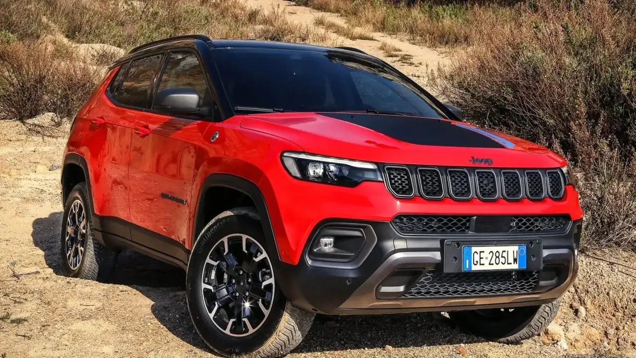 Un Jeep Compass Trailhawk 4xe rojo se aventura por un camino de tierra, listo para explorar.