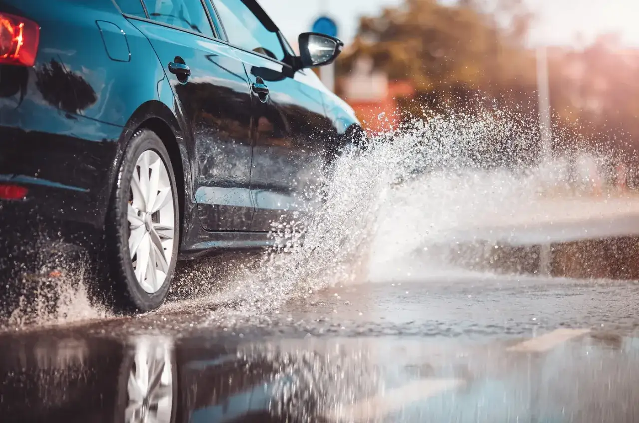 Un coche negro salpica agua al pasar por una carretera mojada.