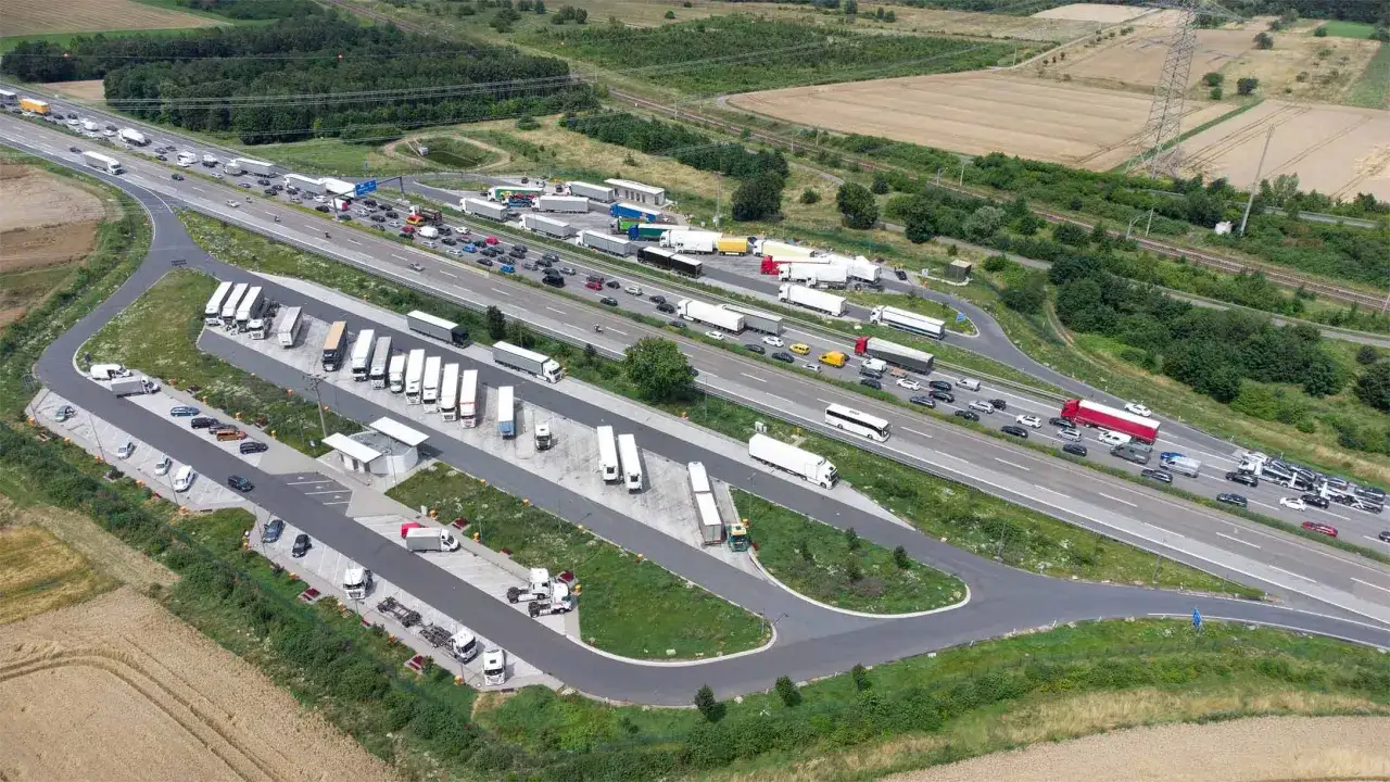 Vista a&eacute;rea de un &aacute;rea de parking camiones con muchos veh&iacute;culos estacionados y tr&aacute;fico en la autopista.