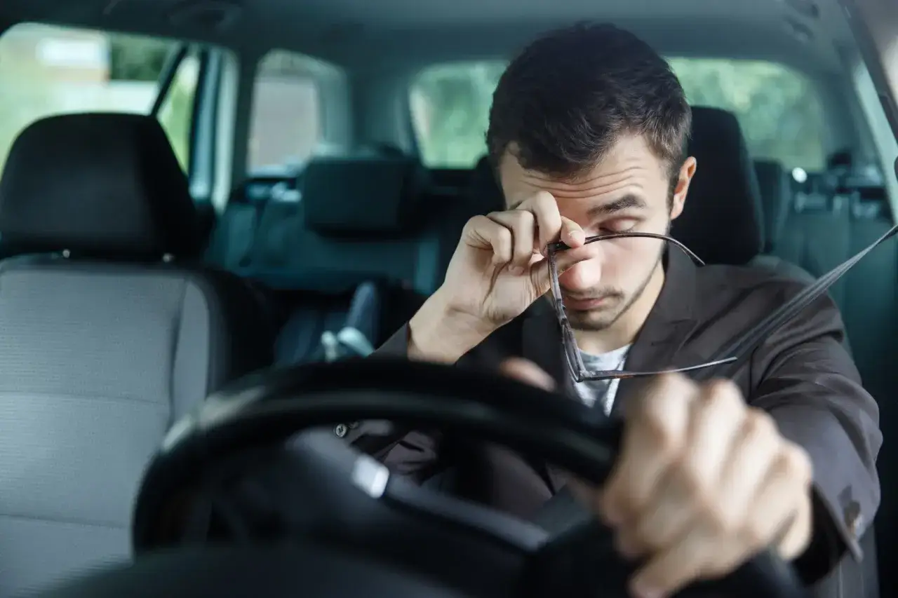 Hombre somnoliento al volante, se frota los ojos. Para disminuir la probabilidad de somnolencia debe evitar conducir.