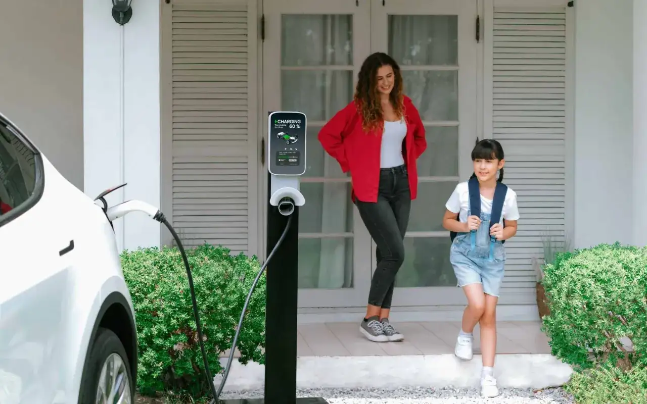Madre e hija salen de casa mientras el coche el&eacute;ctrico est&aacute; en tiempo de carga. La estaci&oacute;n de carga muestra 60%.