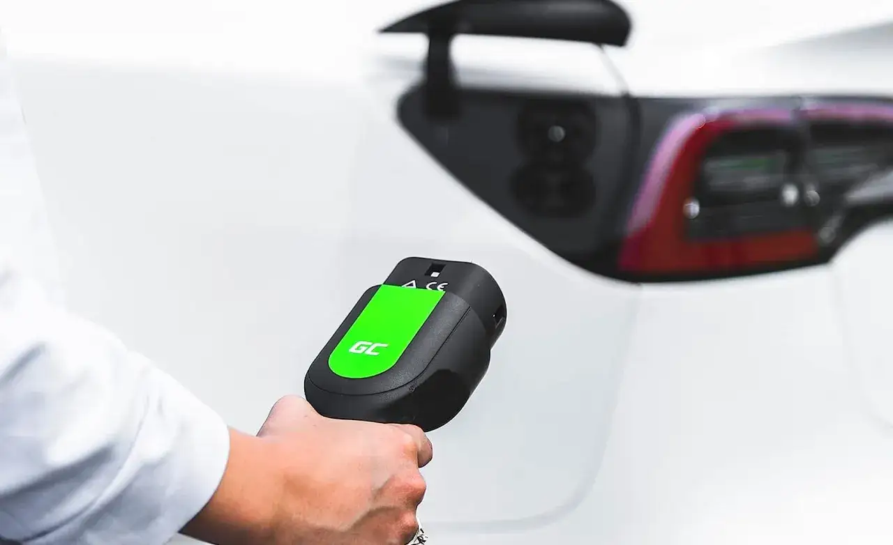 Mano sujetando un cargador de coche el&eacute;ctrico verde y negro, listo para conectar. Averigua cuanto cuesta cargar un coche el&eacute;ctrico en Carrefour.