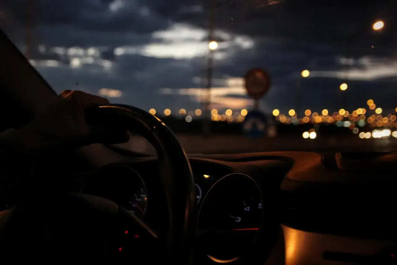 Mano al volante, luces de ciudad de noche. Para no deslumbrar, baja la intensidad del tablero.