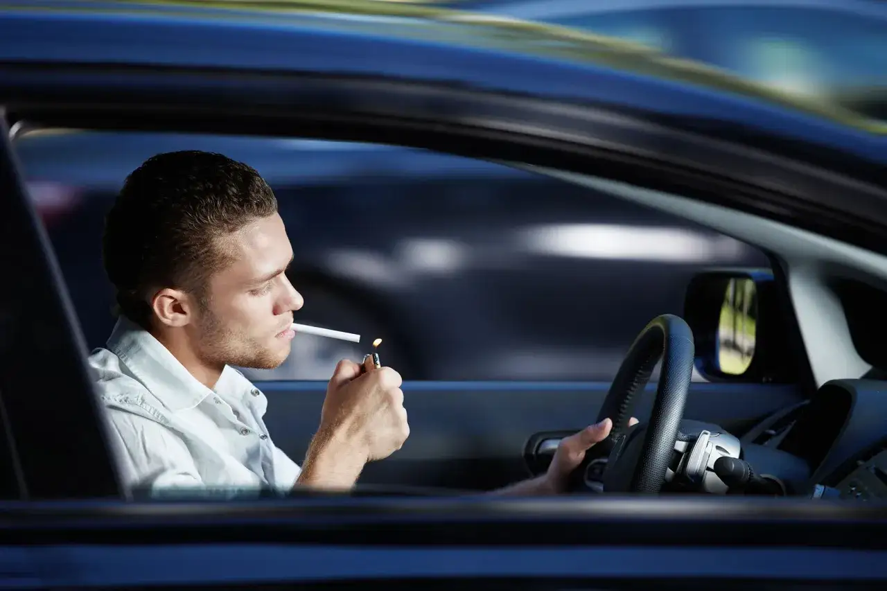 Joven enciende cigarrillo mientras se puede fumar conduciendo.
