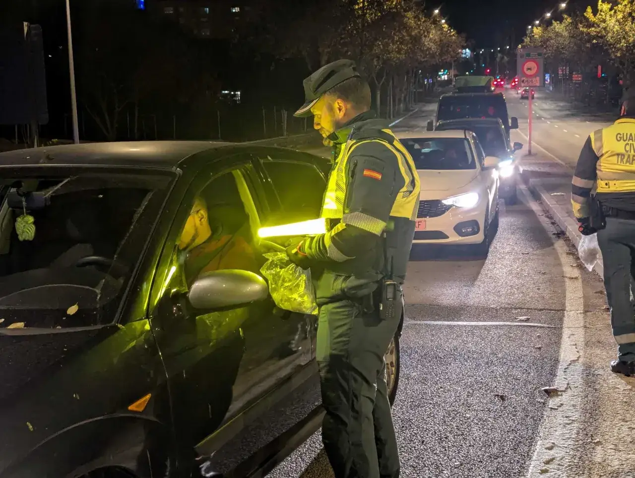 Agente de tráfico realiza control de tasa de alcoholemia a conductor en carretera nocturna.