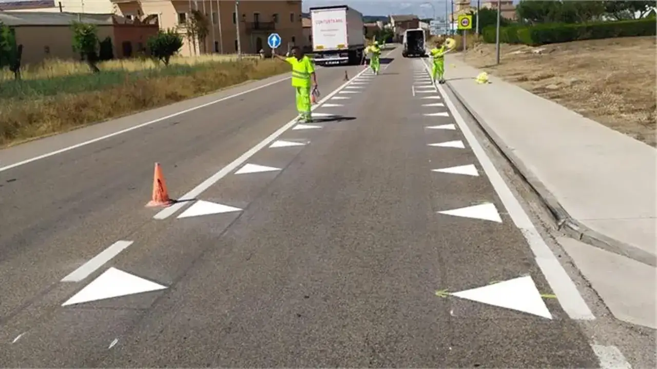 Trabajadores pintan nuevas marcas longitudinales en la carretera, creando un camino seguro con conos naranjas y señalización.