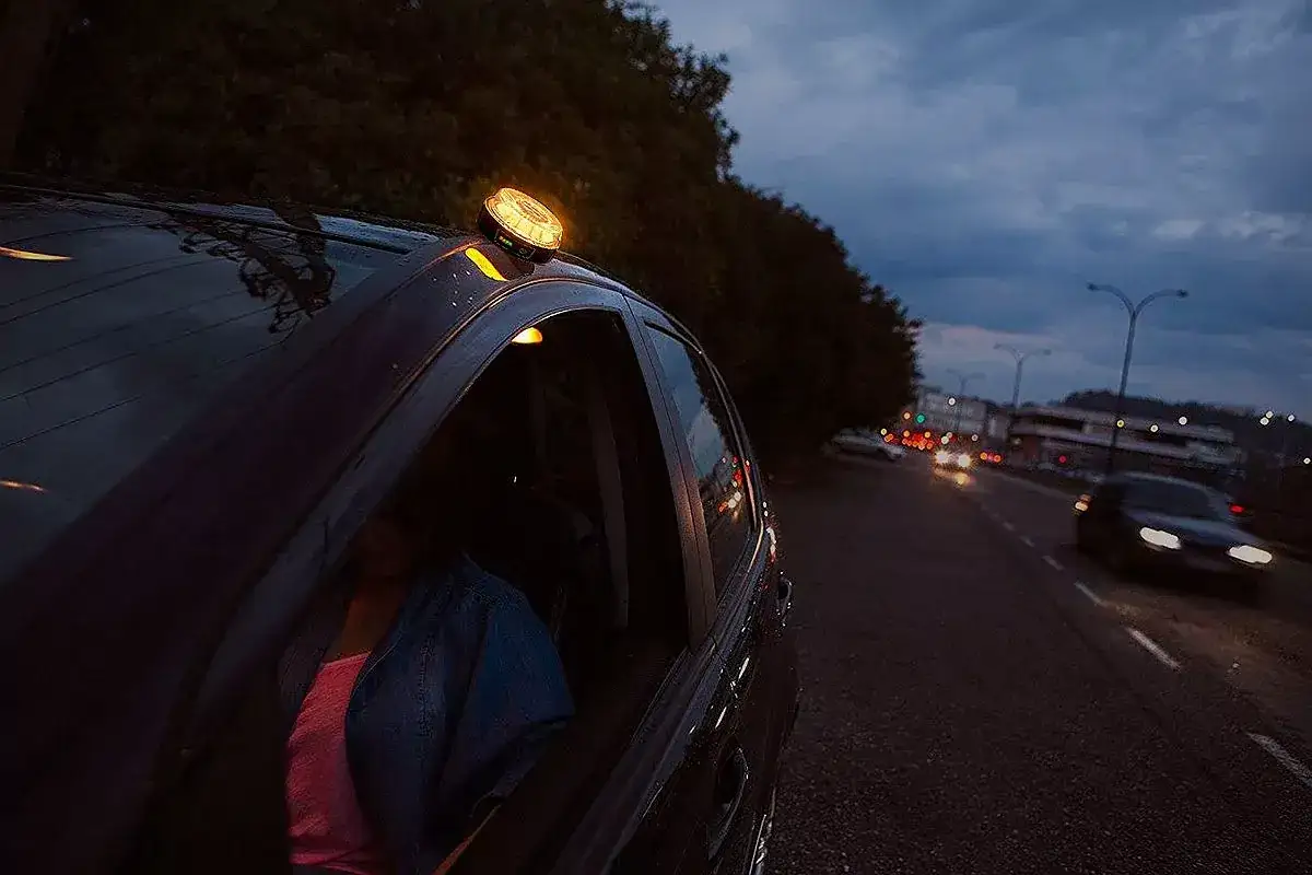 Conductora novel con luz de emergencia en el techo. La noche cae y el tr&aacute;fico avanza.