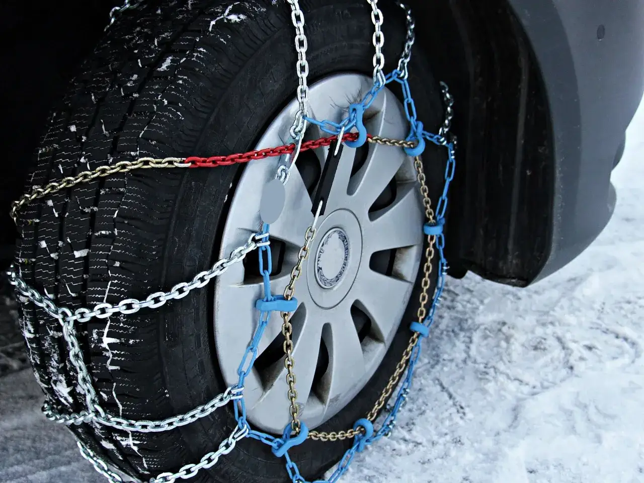 Detalle de c&oacute;mo colocar cadenas de nieve en un neum&aacute;tico cubierto de escarcha, con eslabones plateados y azules.